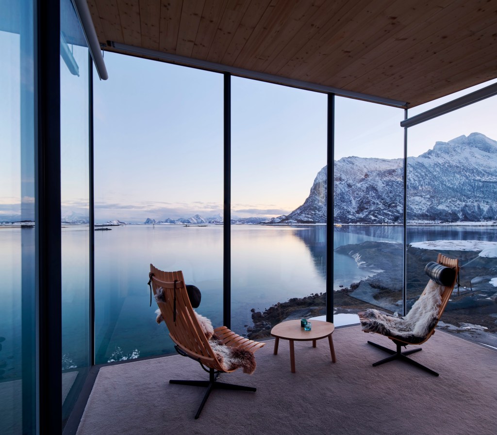 Modern chairs in glass-walled room with water and mountain views