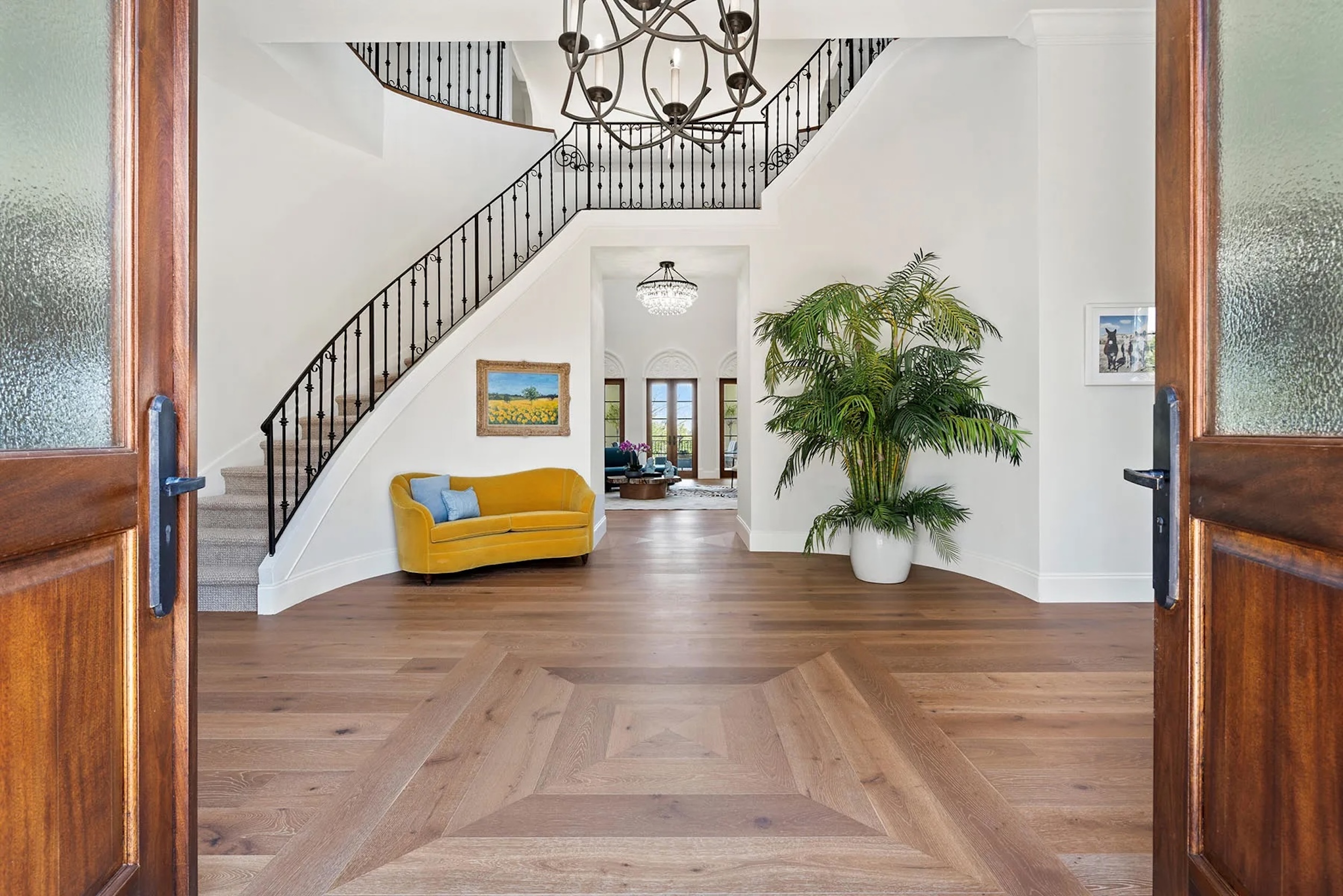 grand staircase and foyer with yellowish couch, plants, and wood floors