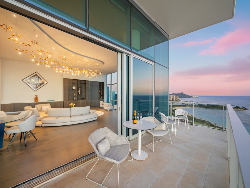 Balcony of a home in Honolulu, Hawaii with views through glass walls into the living room.
