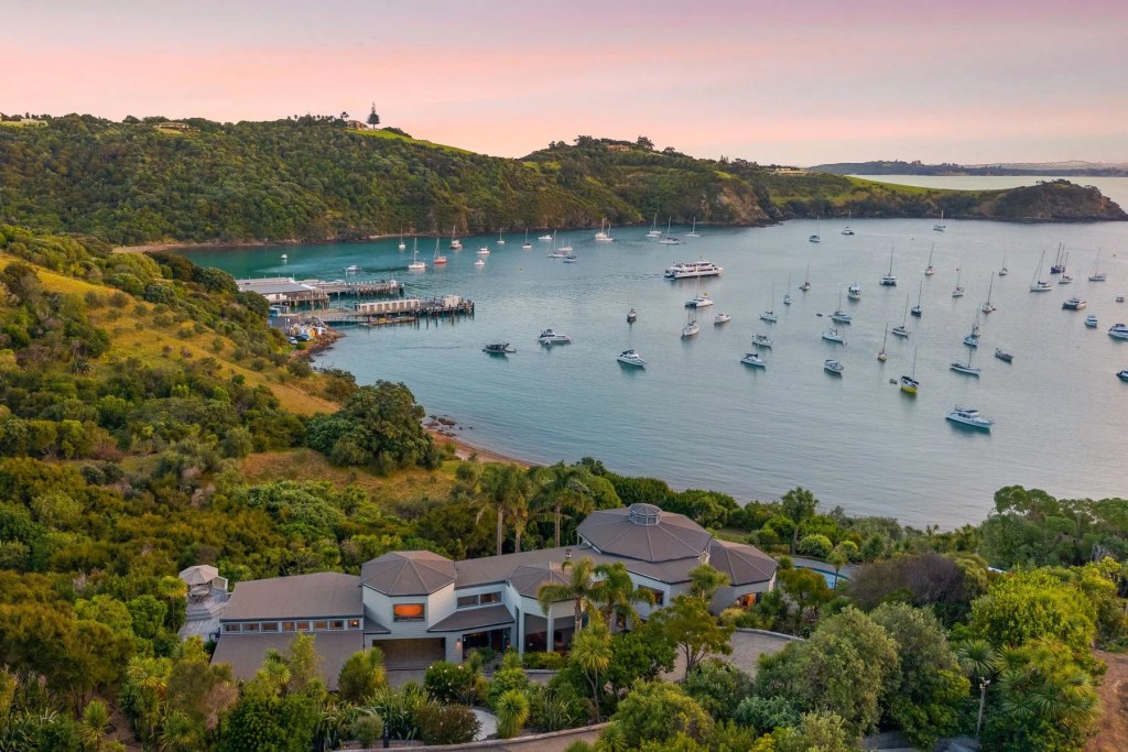 View of a home in the lower foreground at sunset with a harbor and boats on Waiheke Island, New Zealand.