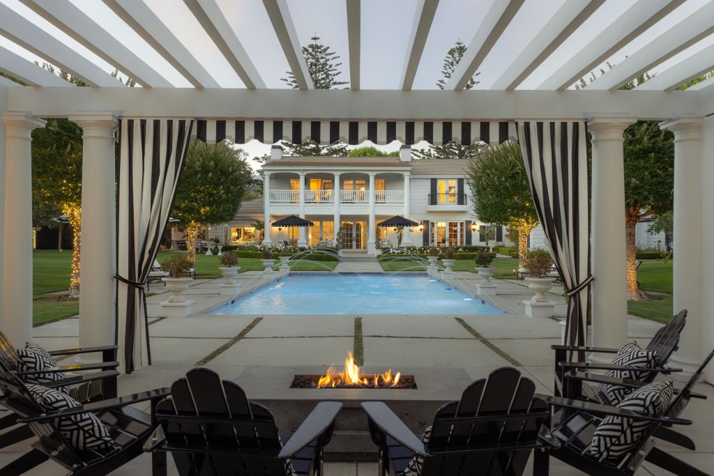 fire pit underneath a pergola facing the pool, terraces, and back of home exterior