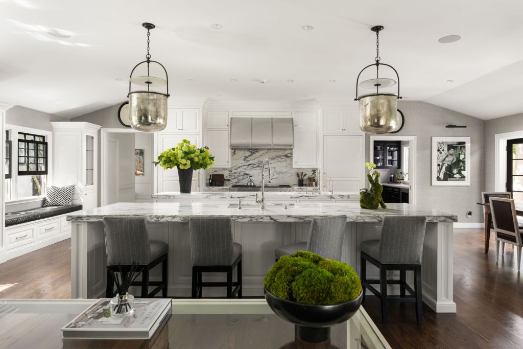 grey and white kitchen with dual marble islands, marble oven backsplash, and window seat