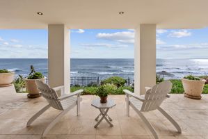 Private covered terrace with Adirondack seating and unobstructed ocean views, overlooking landscaped grounds and the shoreline.