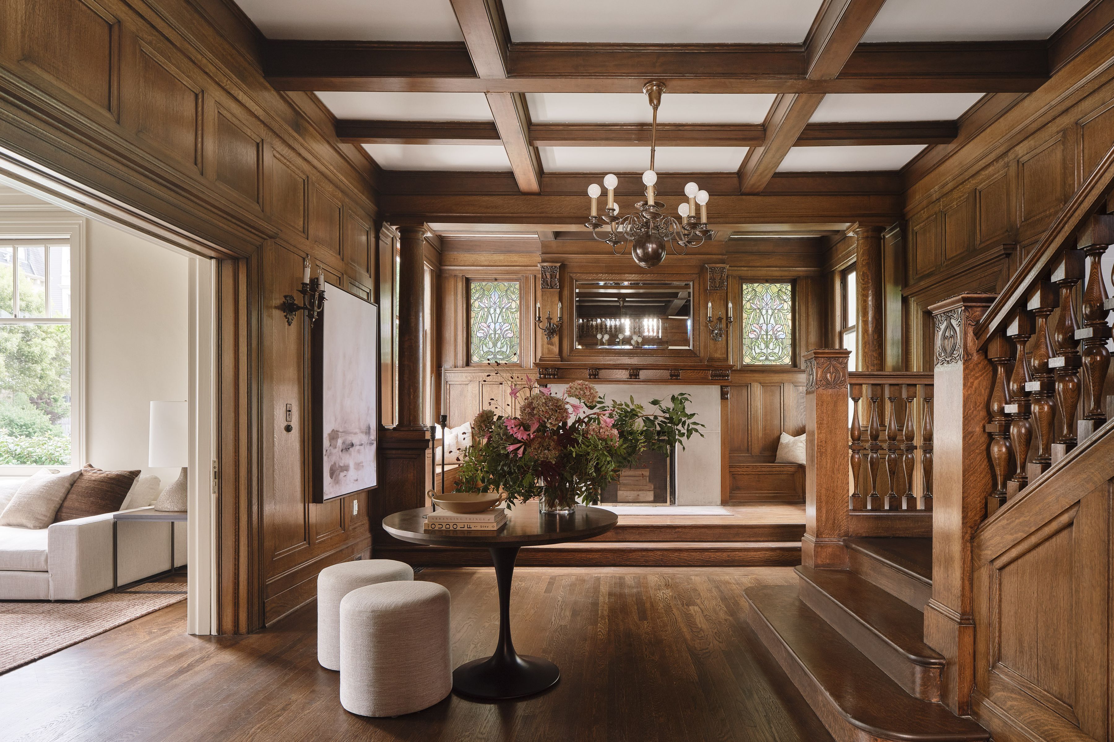 interior of wood paneled foyer in Presidio Heights home with side table and two stools, art on the walls, grand staircase, and fireplace in background