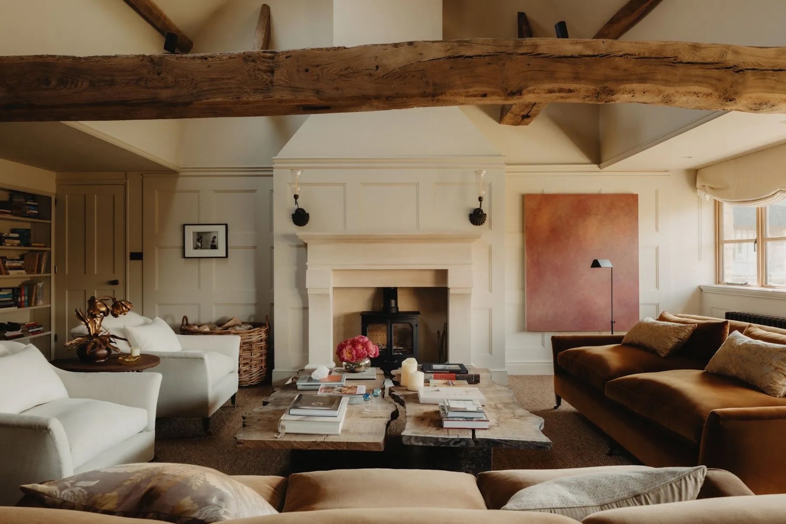 sitting room in Cotswold's home, with rough exposed wood, stone fireplace, and plush seating surrounding two coffee tables with stacked books