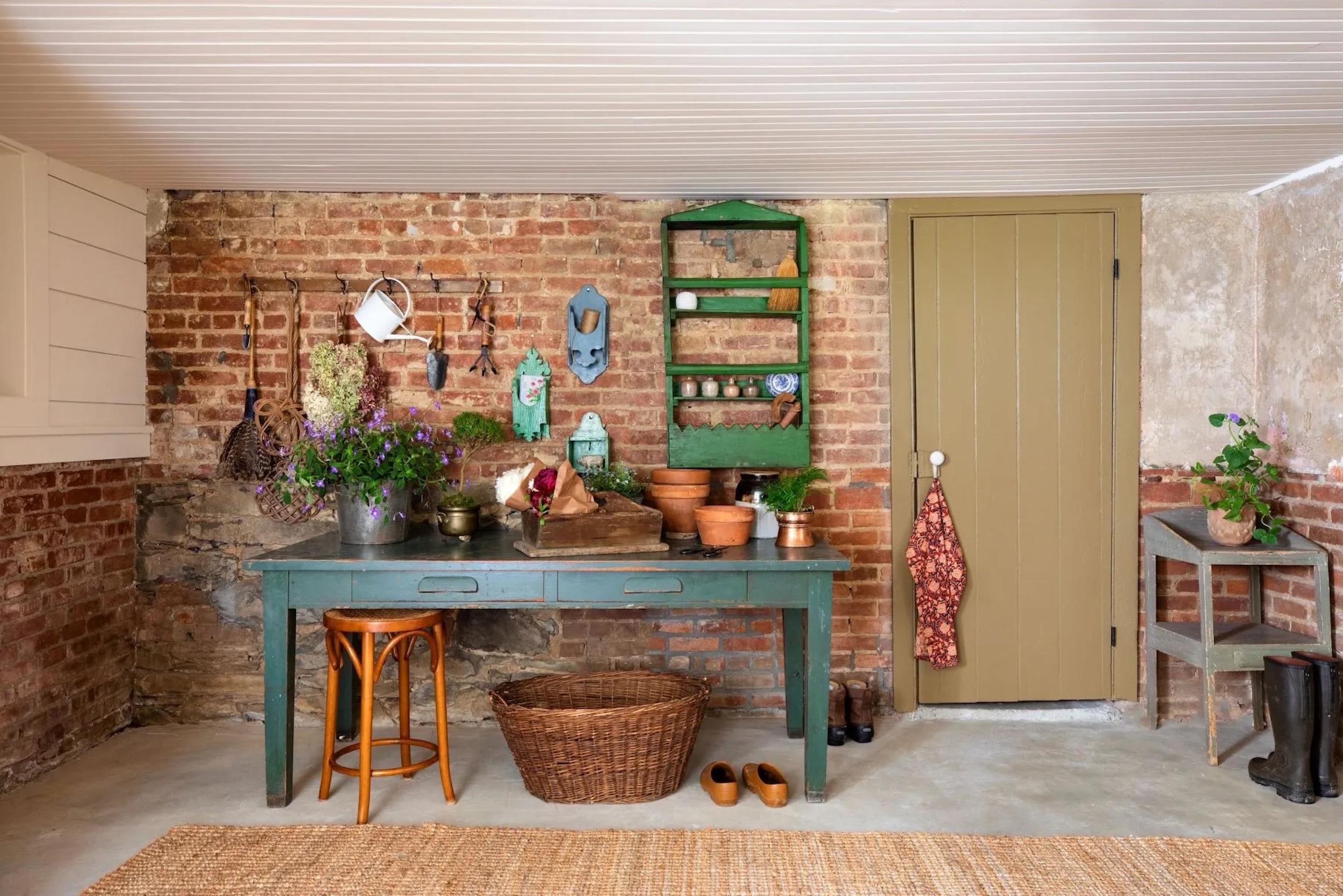 potting/ gardening space in Hudson Valley, New York home, with rustic tables and shelving, gardening tools on brick facade wall