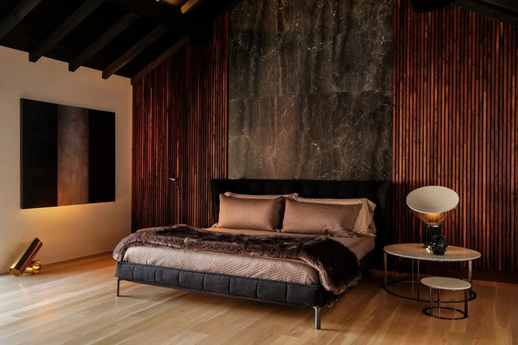 moody bedroom in Portland, Oregon home with large tapestry against fluted wood walls, artistic light fixtures, and layered bedding