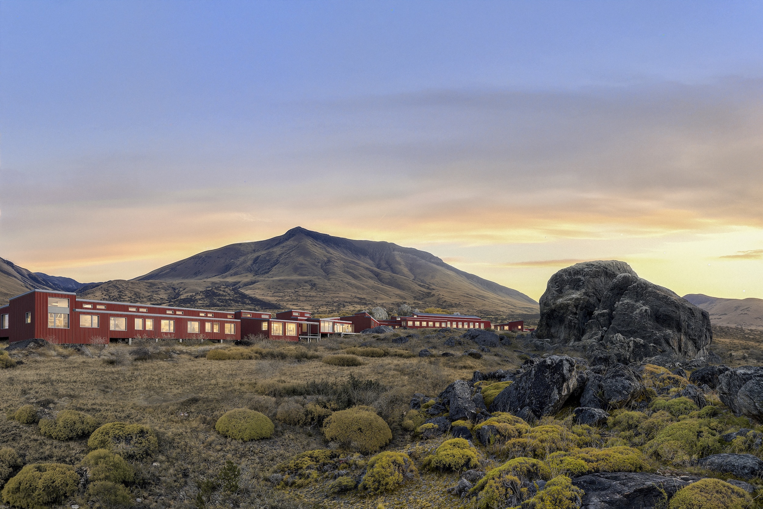Exterior of Explora El Calafate with sunset and mountains in the background, rugged terrain in the foreground