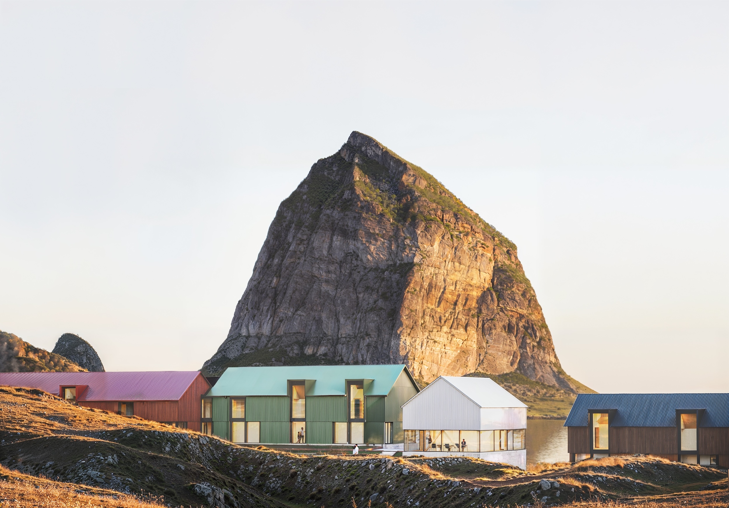exterior of Ytir, a retreat on a Norwegian island, showcasing four buildings and a rugged landscape with large cliffside rock in the background