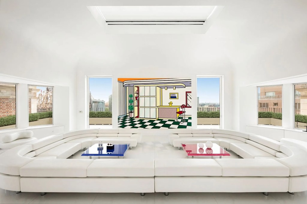 all white salon in New York City apartment with large u-shaped seating with red and blue coffee tables and pop art on the wall behind, with windows on either side