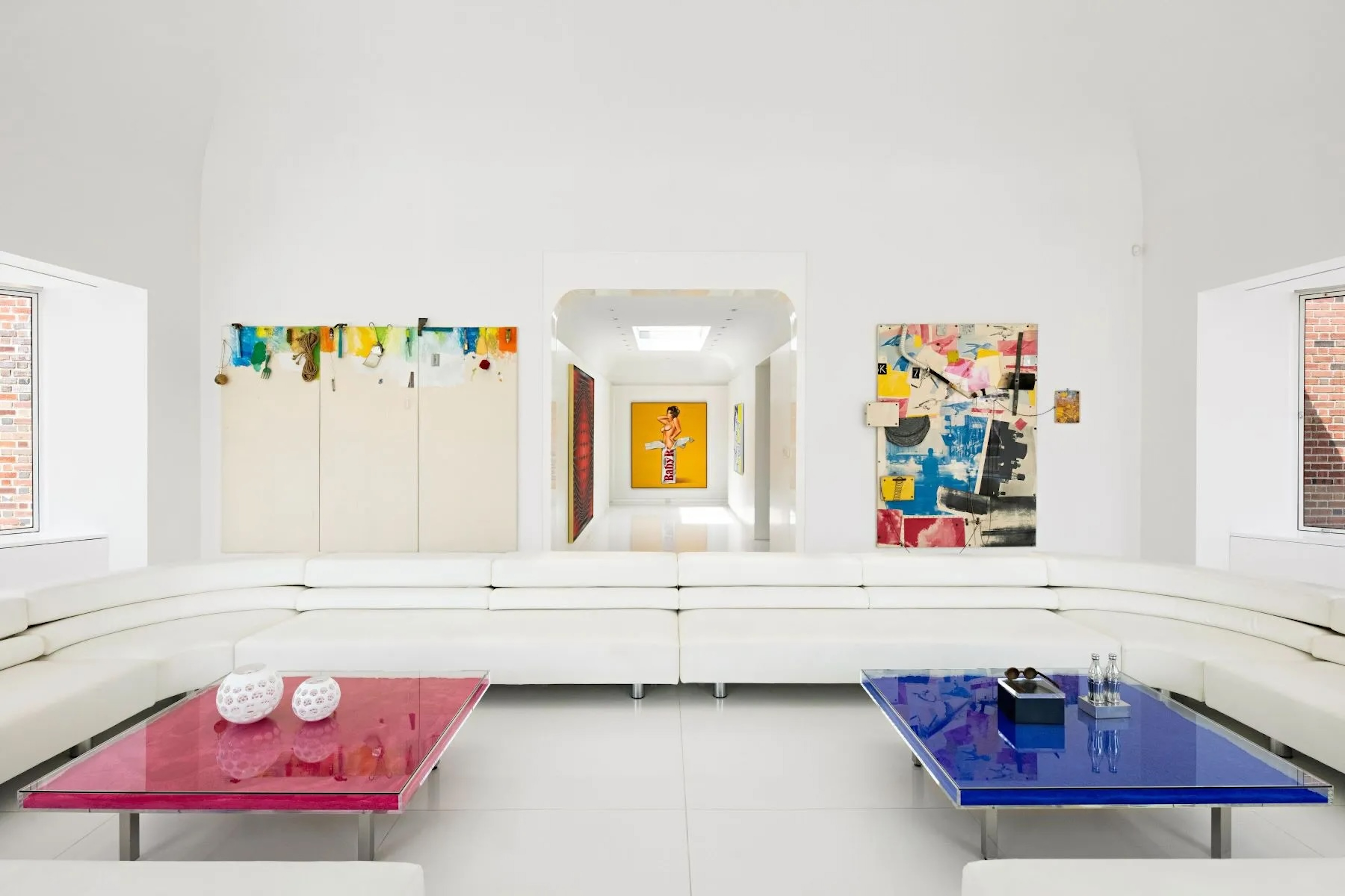 monochromatic salon with statement seating, red and blue coffee tables, and exquisite art collection on walls behind