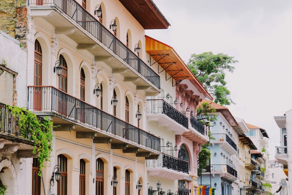 Historic architecture in Panama City's Casco Viejo district, showing multi-story buildings with wrought-iron balconies, arched windows, and colorful facades lining a narrow street.