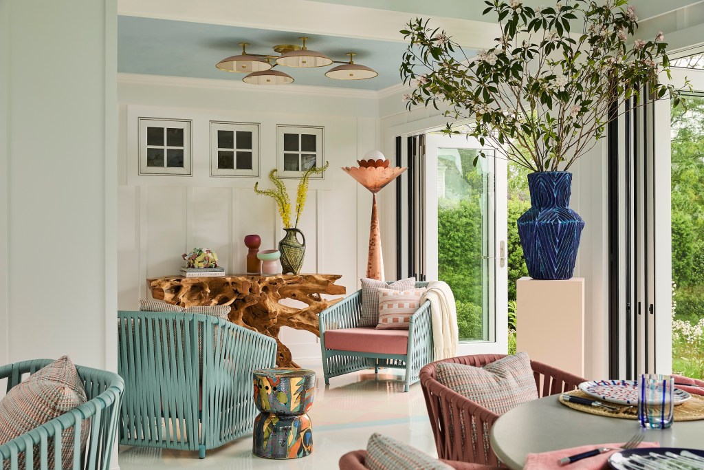 photo of indoor/ outdoor space designed by Phillip Thomas, featuring brightly colored ceramics, a natural abstract wood console table displaying various other ceramic pieces and books, surrounded by turquoise and pink seating