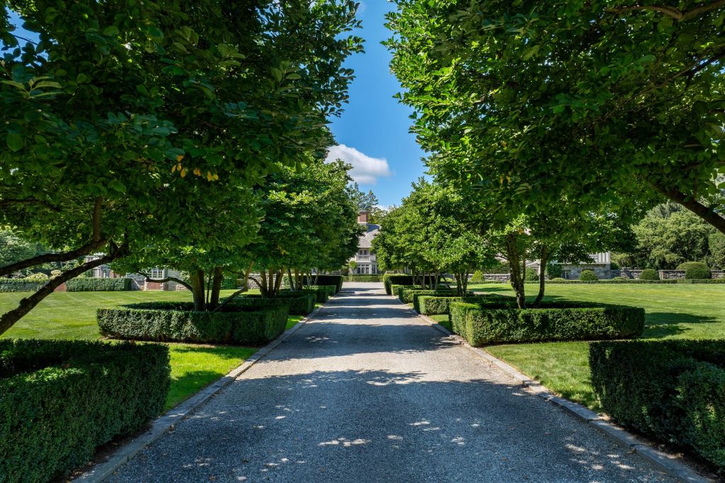 white-pebble driveway, with boxwoods, magnolia trees, leading toward a Tudor-style home in Greenwich, CT