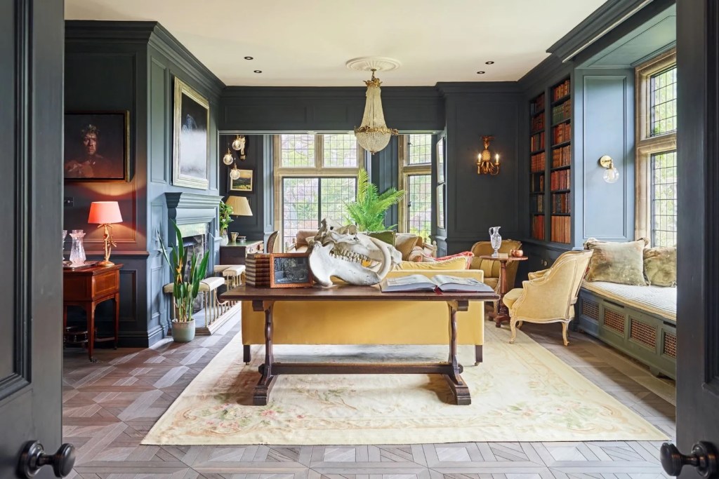 ornate sitting room with dark walls in Wiltshire England, with a large fossilized bone on a console table next to an open book and frame, and ornate furniture in the background, with a crystal chandelier