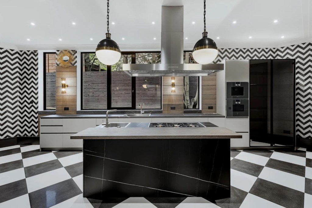 kitchen in London with black stone island, grey marble countertops, white cabinets, black appliances, and black and white chevron walls