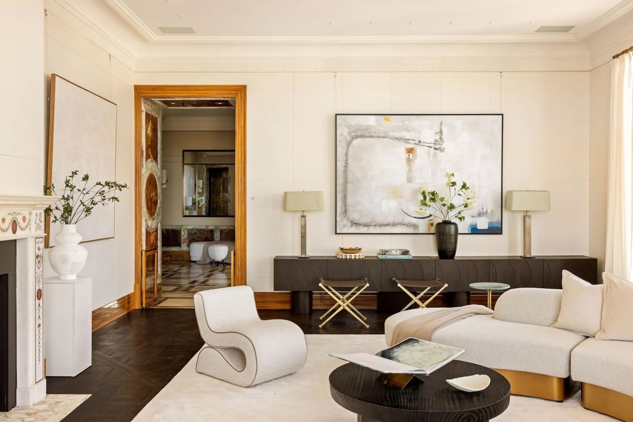 monochromatic home with white sculptural seating, gold accents, and dark wood console table, coffee table, and floors. wall with art in the background